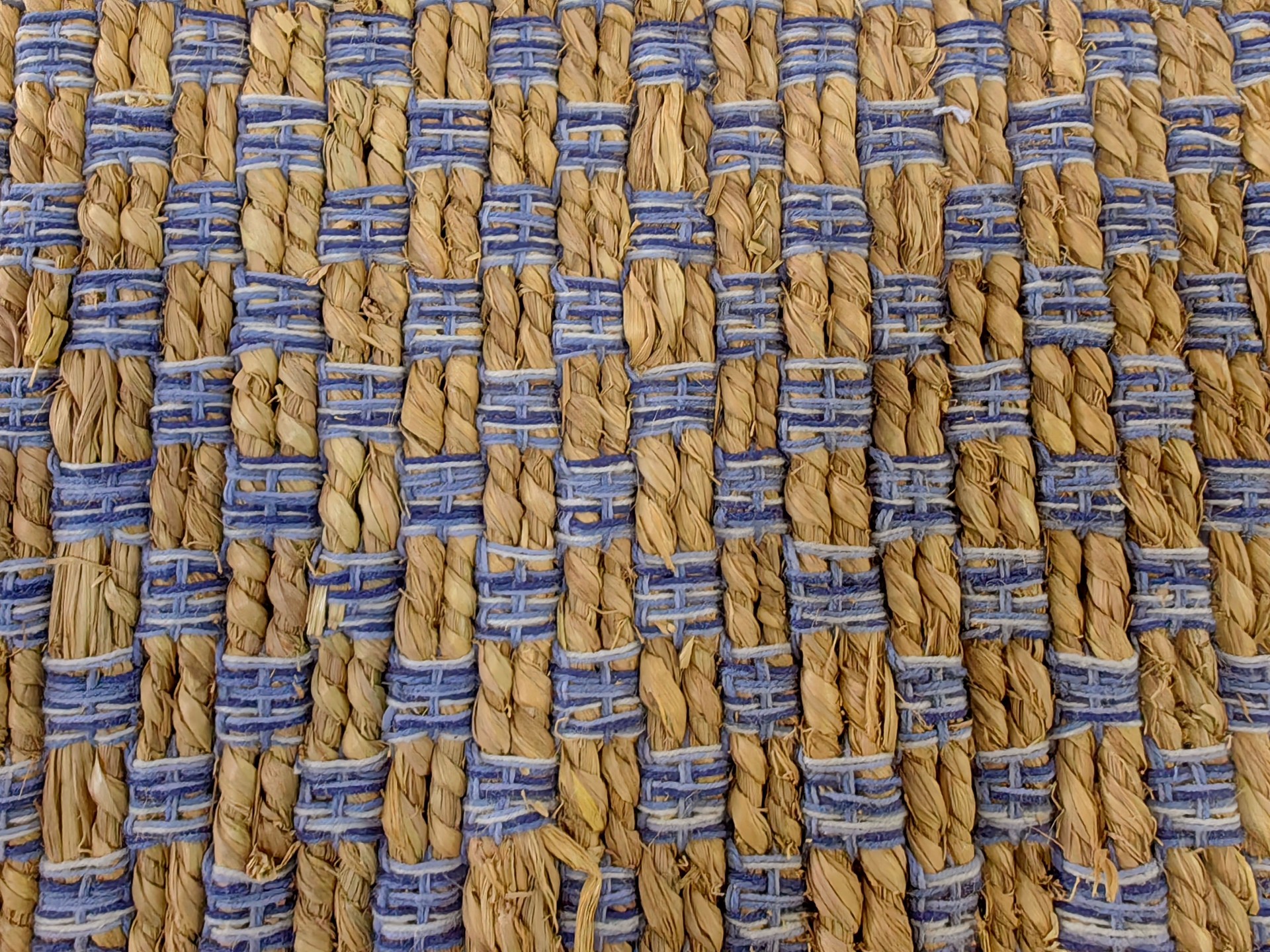 woven carpet displaying intricate patterns natural fibers in muted colors and blue accents. closeup.